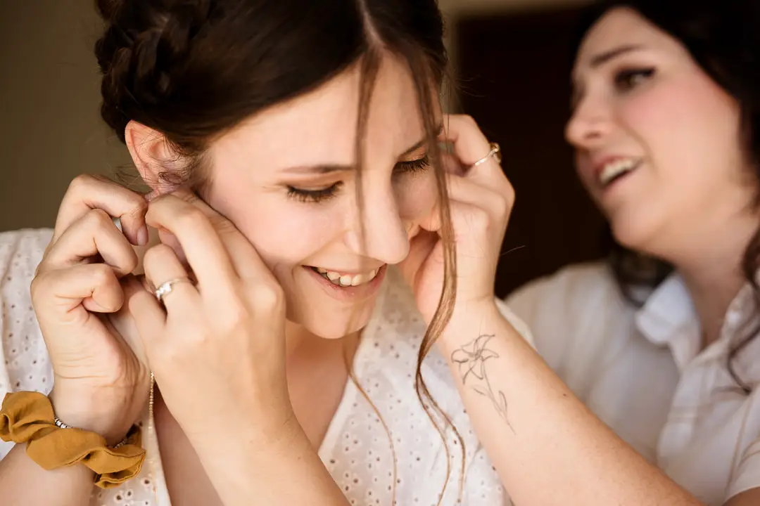 Sposa sorride mentre indossa gli orecchini durante i preparativi