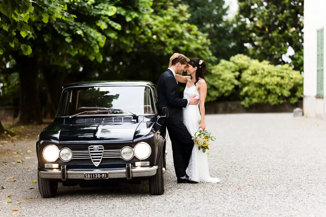 Sposi si abbracciano davanti a un’auto d’epoca a Villa Antona Traversi